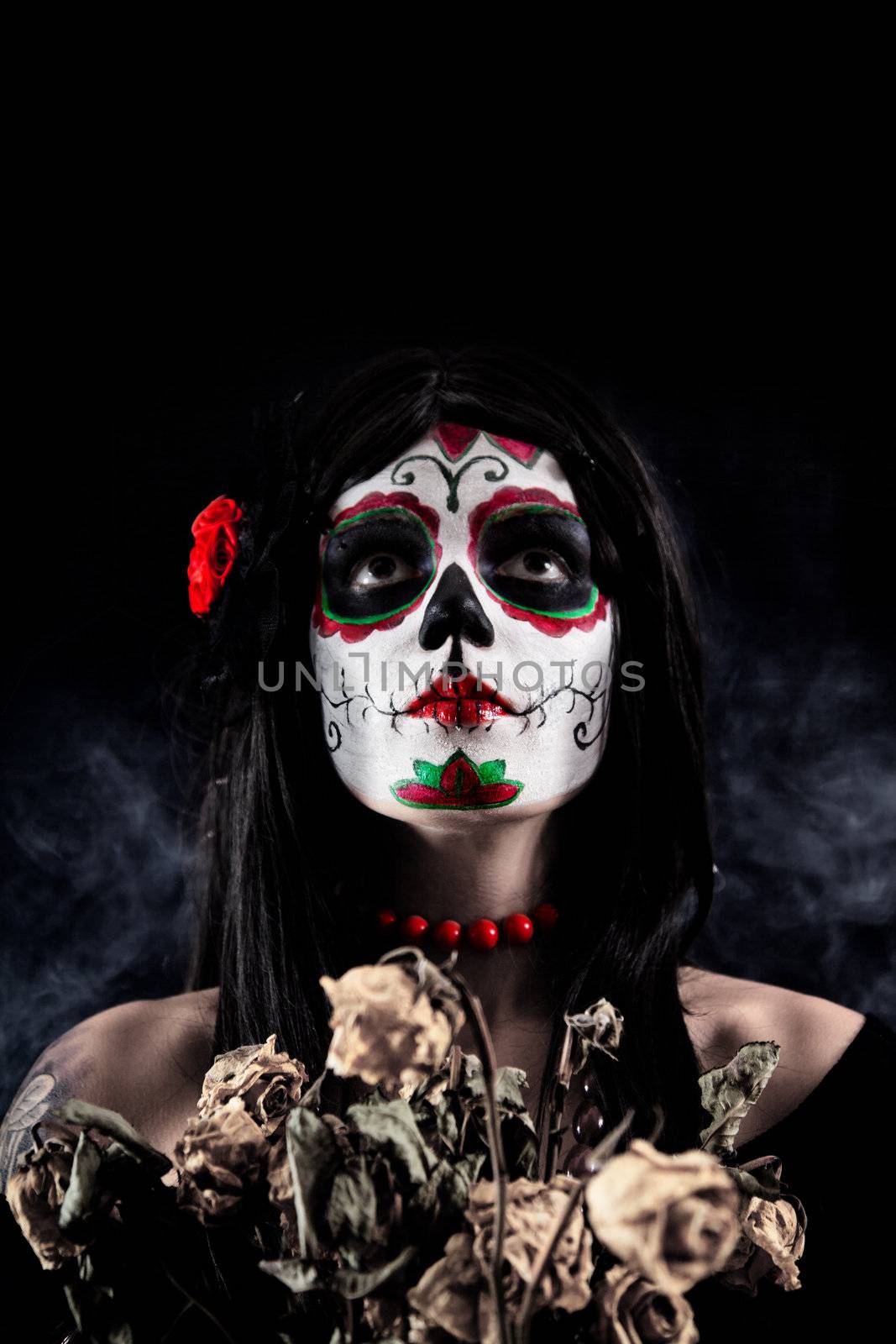 Sugar skull girl with dead roses, studio shot over black smoky background 