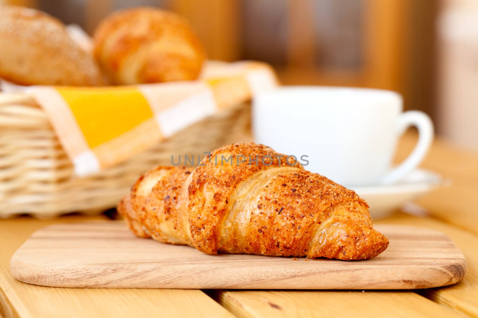 Fresh croissant and white cup coffee, on a wooden table