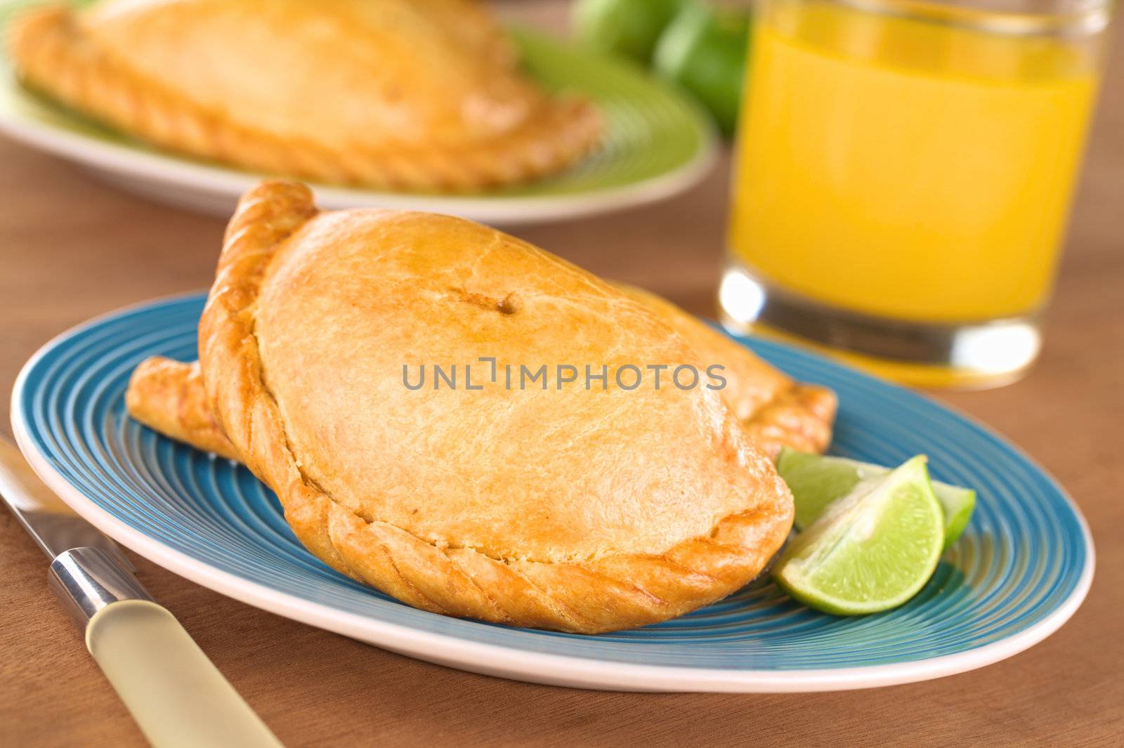 Peruvian snack called Empanada (pie) filled with chicken and beef served with limes (Selective Focus, Focus on the middle front part of the empanada)