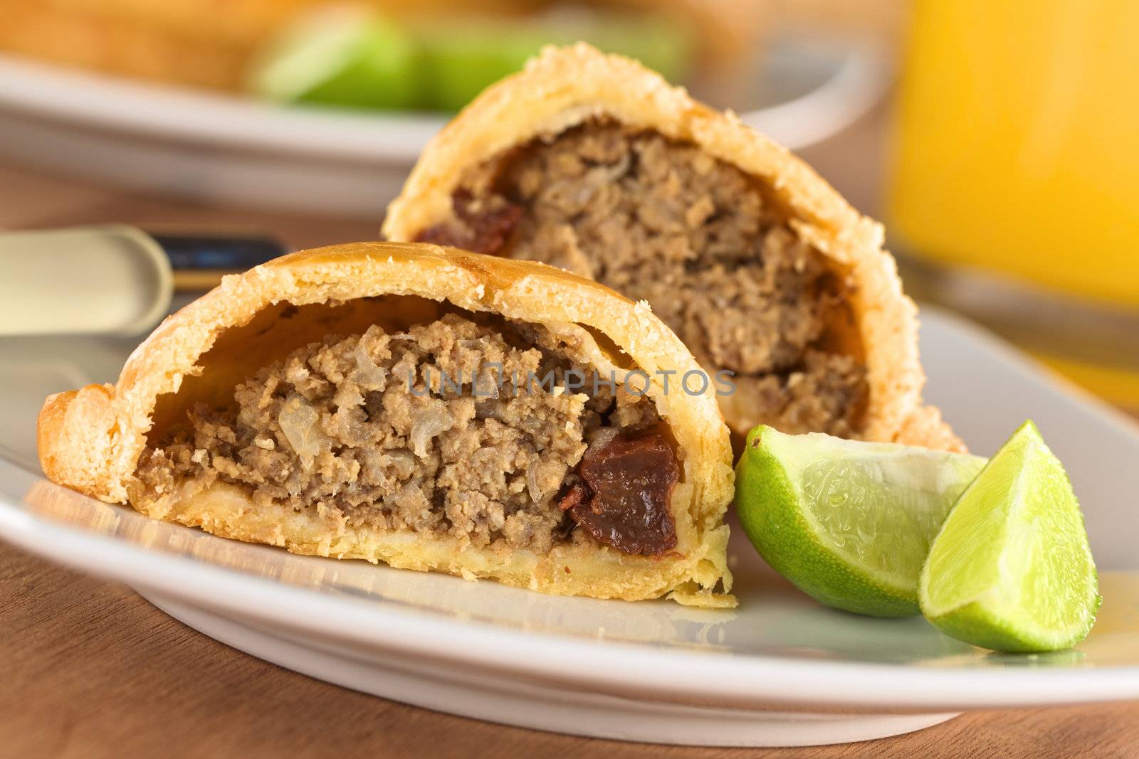 Peruvian snack called Empanada (pie) filled with beef and raisin served with limes (Selective Focus, Focus on the empanada stuffing in the front)