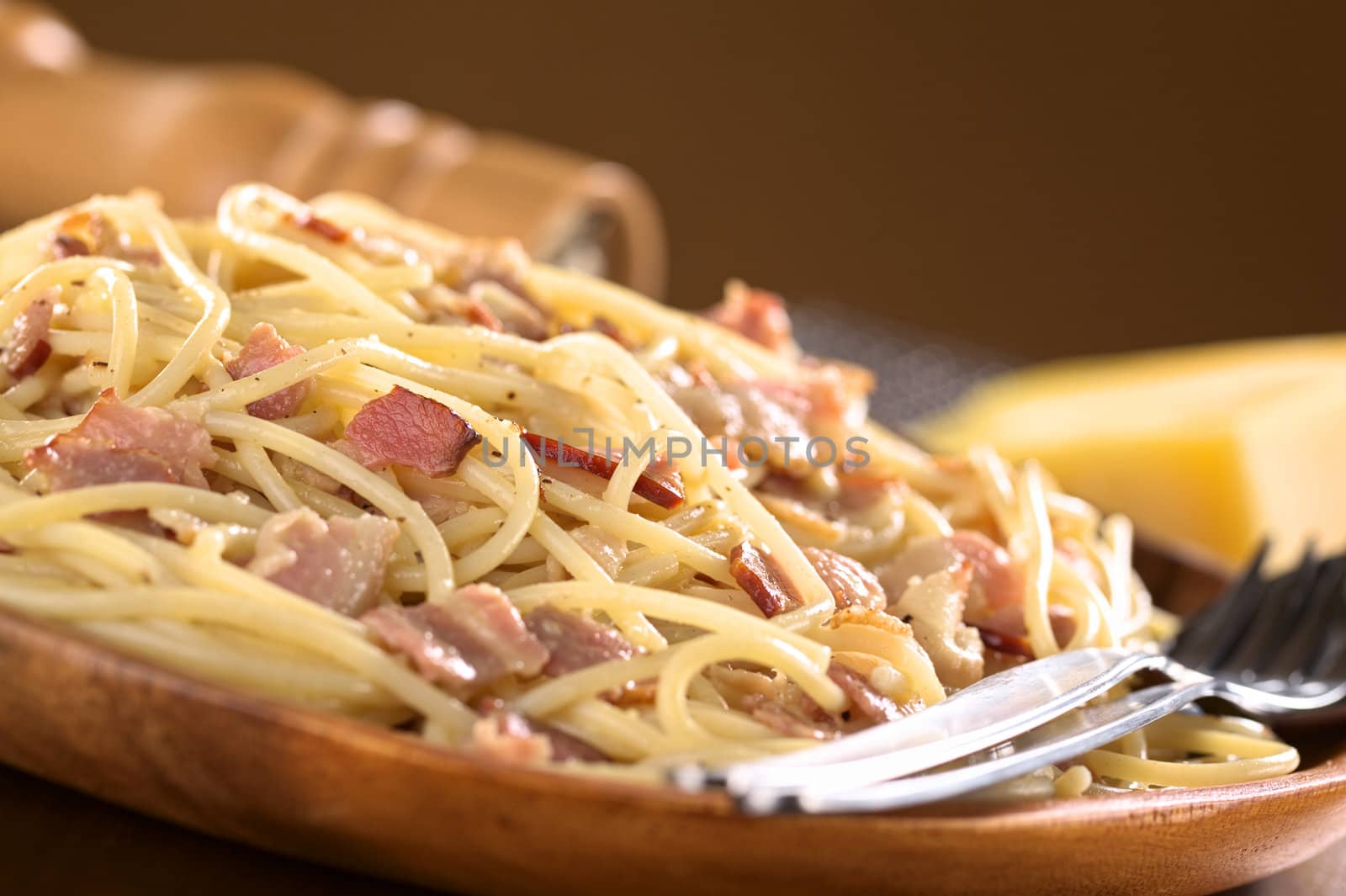 Spaghetti alla Carbonara served on wooden plate (Selective Focus, Focus one third into the meal)