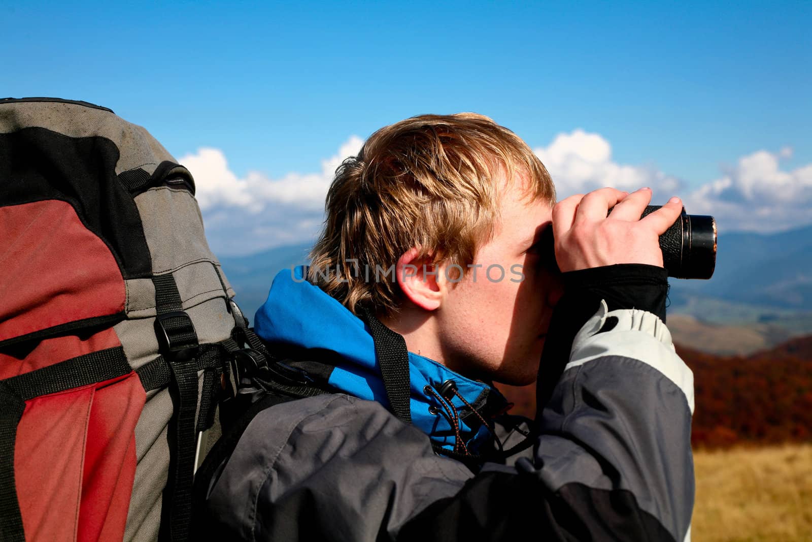 An image of a man walking in mountains. Looking in binoculars