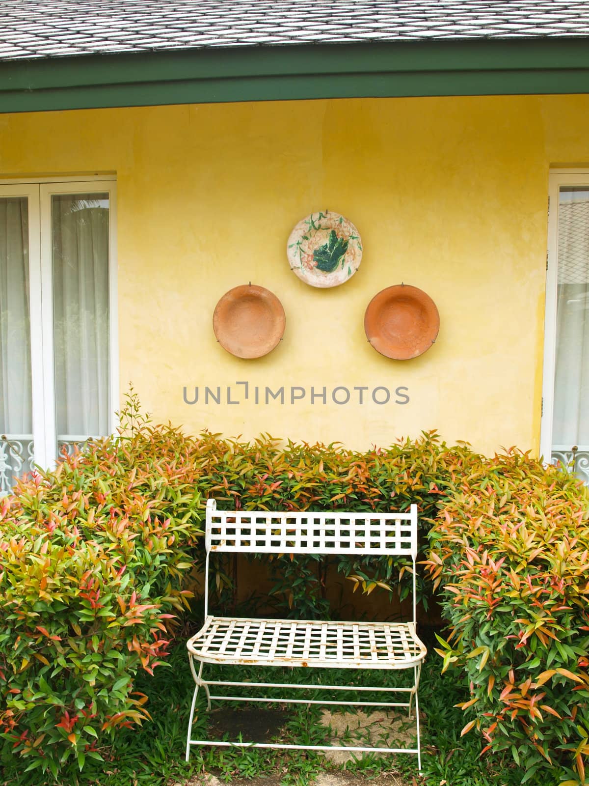 A metal bench in a garden on yellow wall background by gururugu