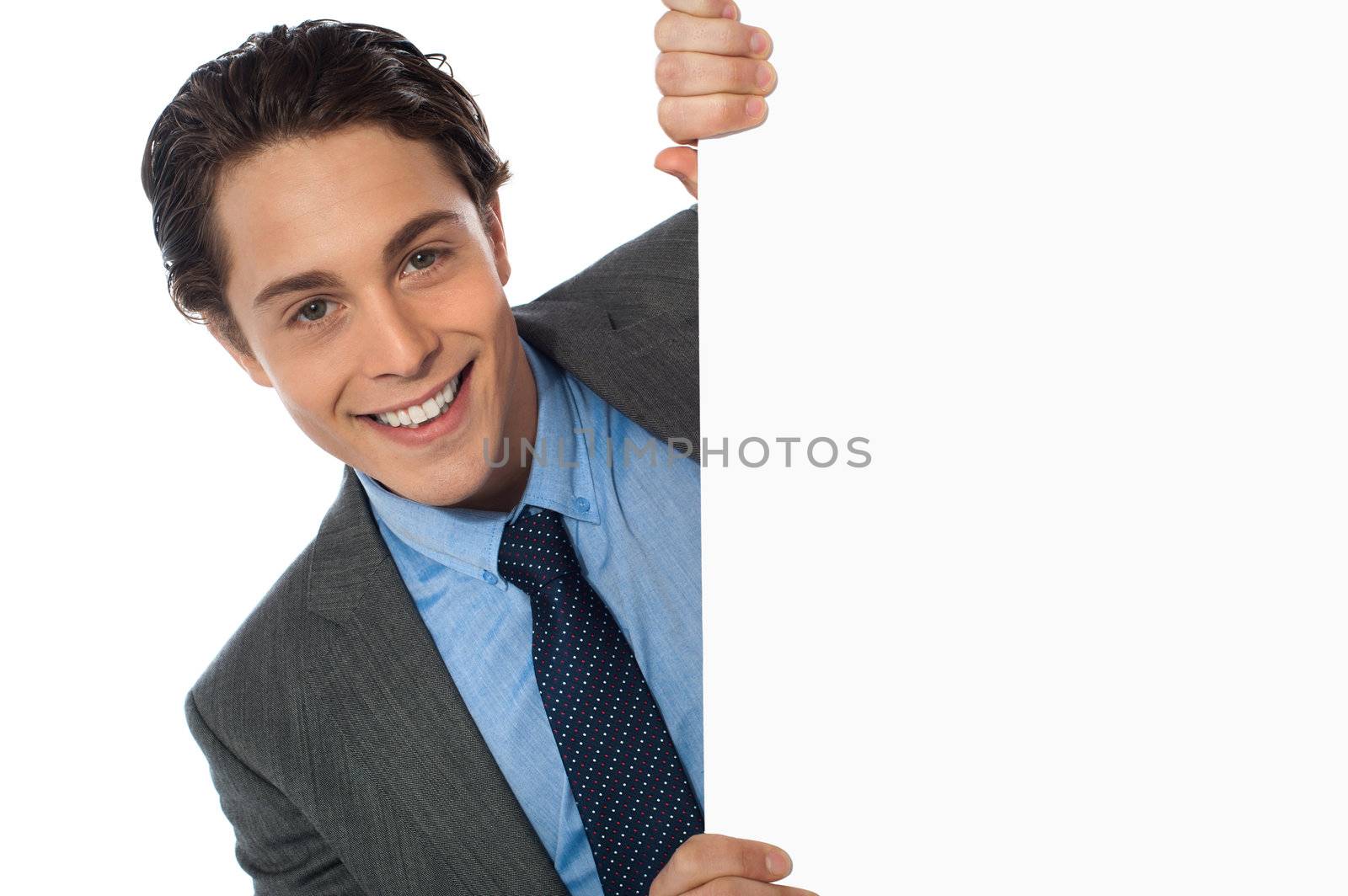 Businessman peeking behind a whiteboard smiling at camera