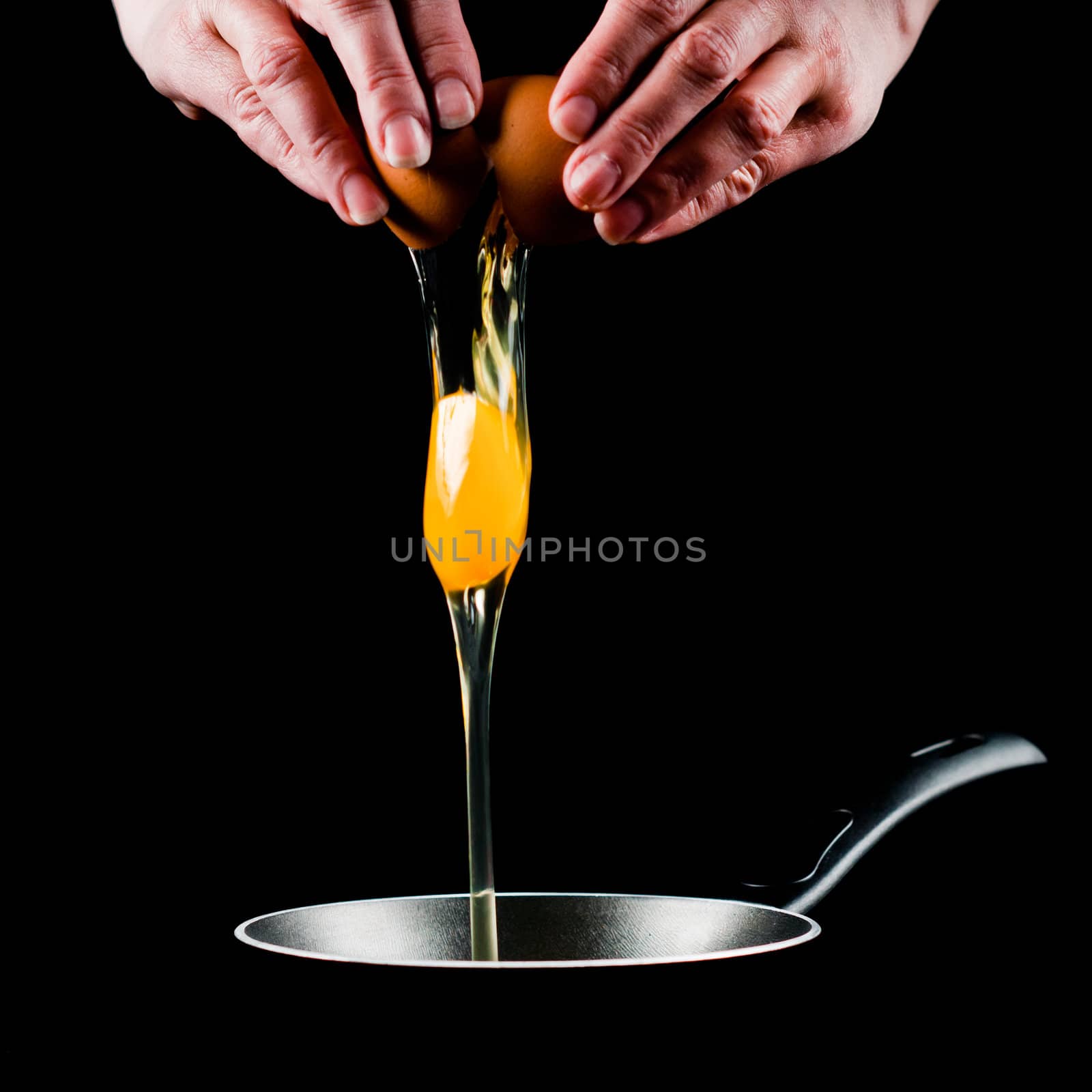 Yolk dropping in pan from cracked raw egg, divided by woman hands