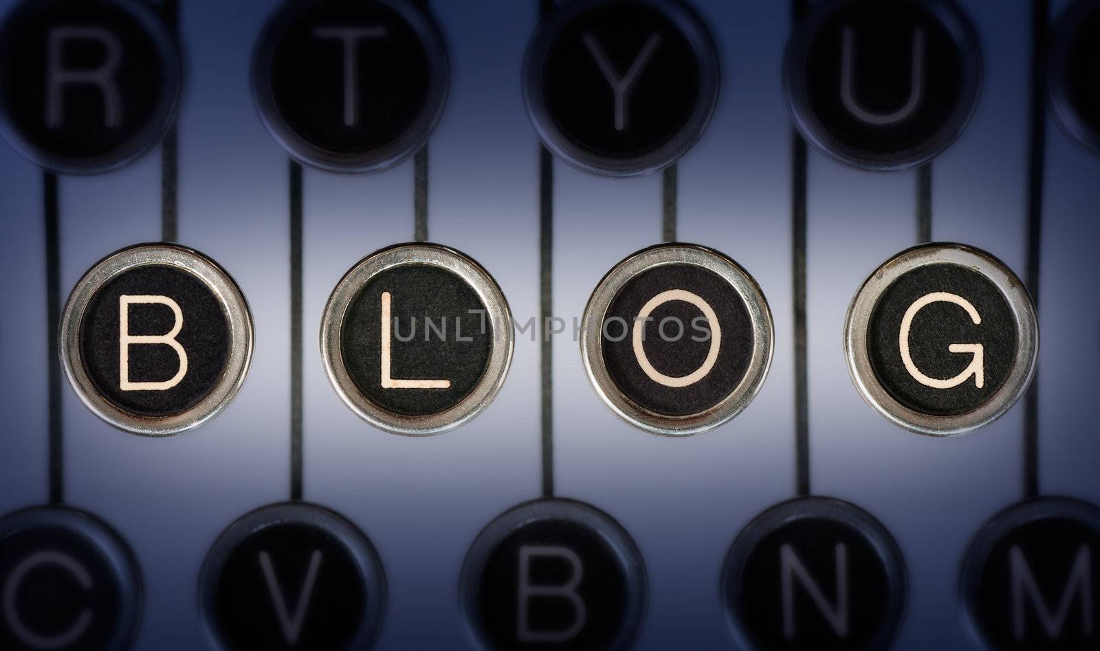 Close up of old typewriter keyboard with scratched chrome keys that spell out the word BLOG Lighting and focus are centered on BLOG 