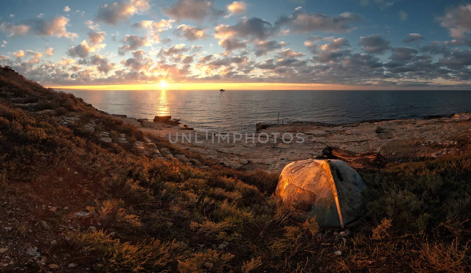 Beautiful seascape on sunrise with old boat on coast and clouds on background