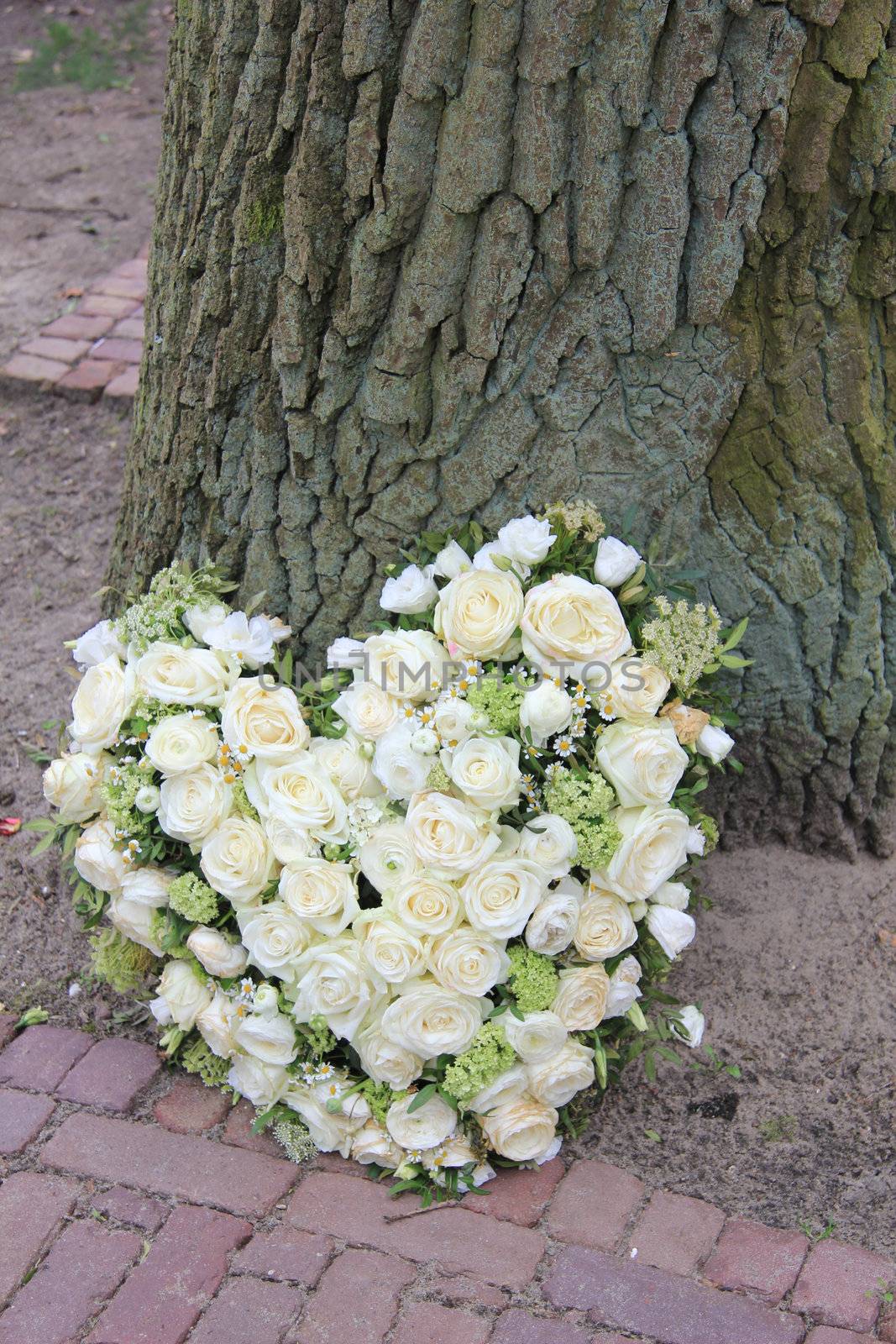 A sympathy flower arrangement near a tree in the shape on an heart