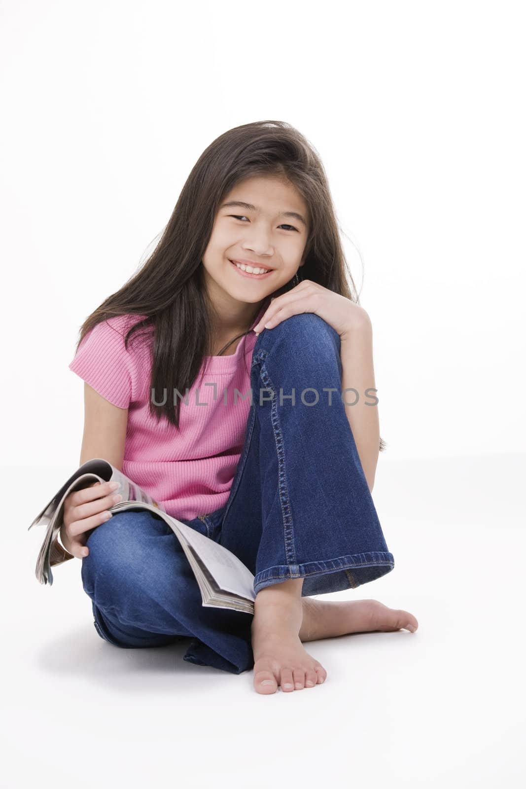 Ten year old Asian girl sitting on floor reading a magazine, isolated on white