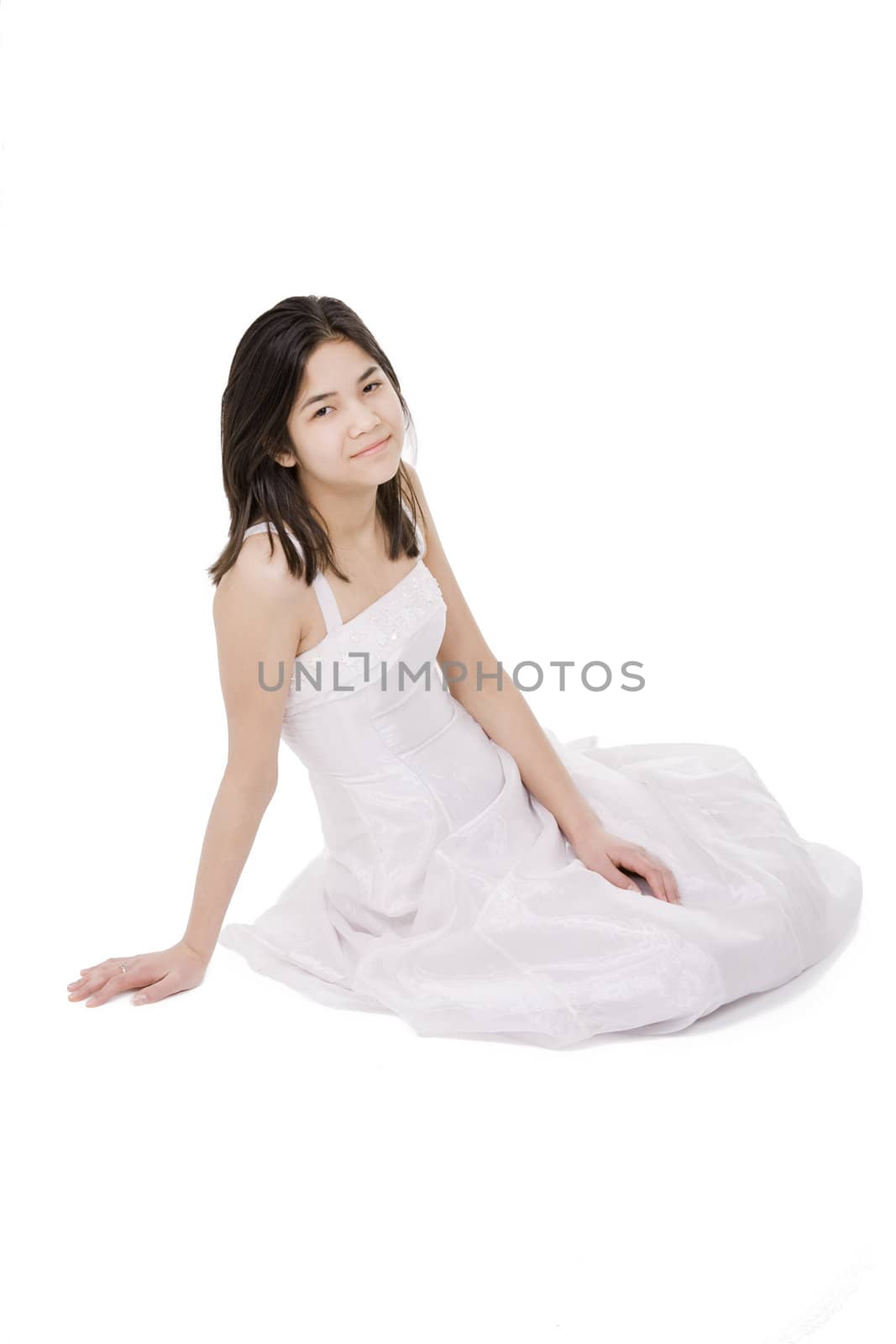 Beautiful young teen girl in white dress or gown sitting on floor, isolated on white