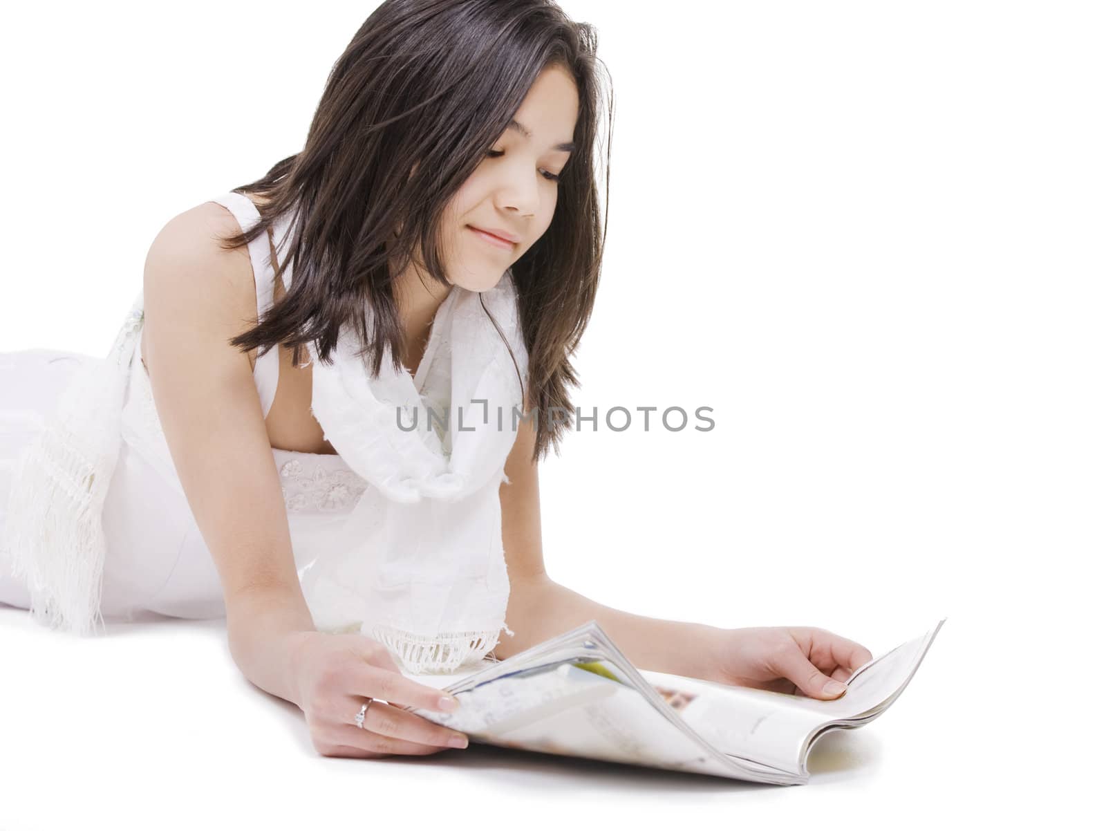 Beautiful young teen girl in white dress or gown lying down reading a magazine, isolated on white