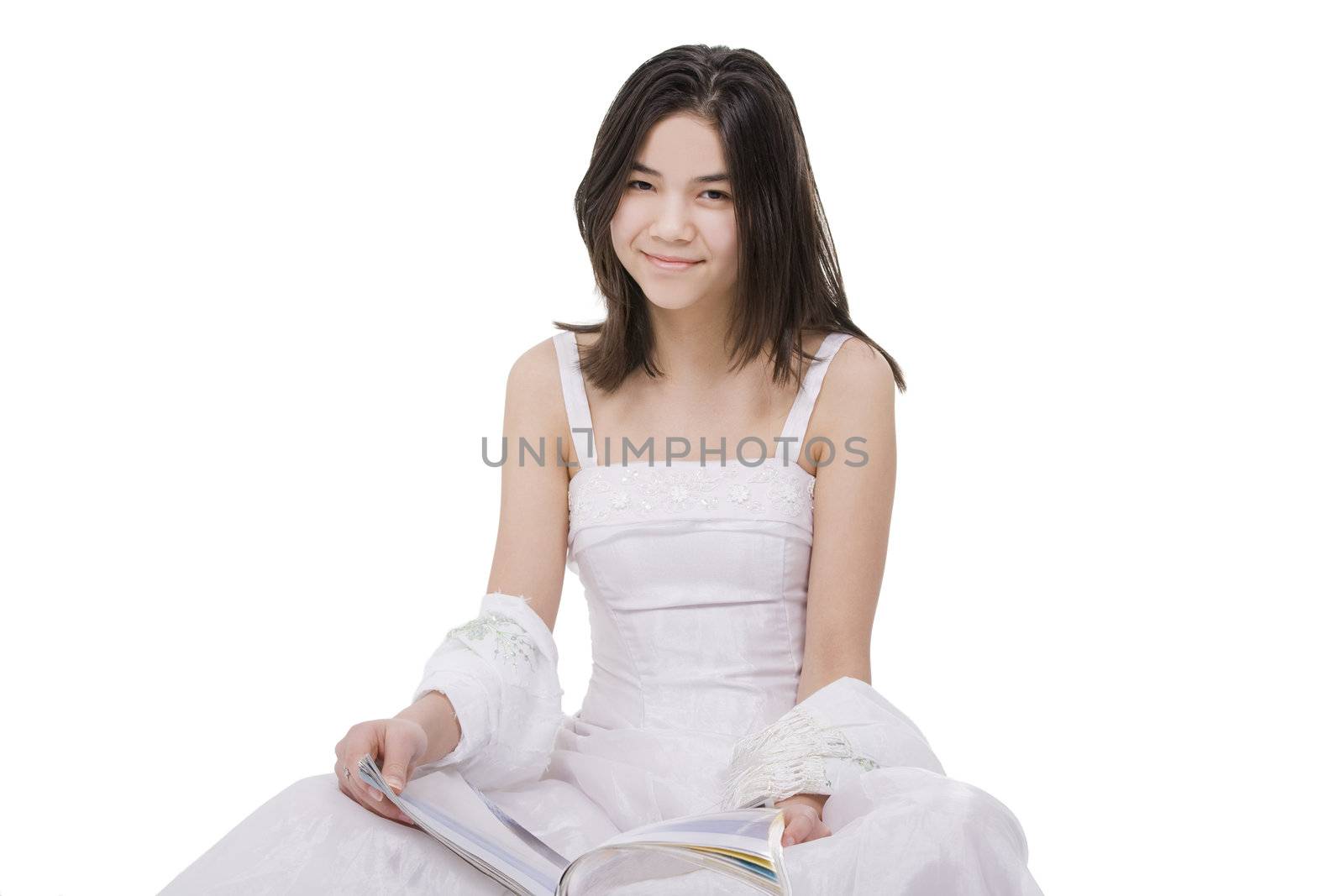 Beautiful young teen girl in white dress sitting reading a magazine, isolated on white