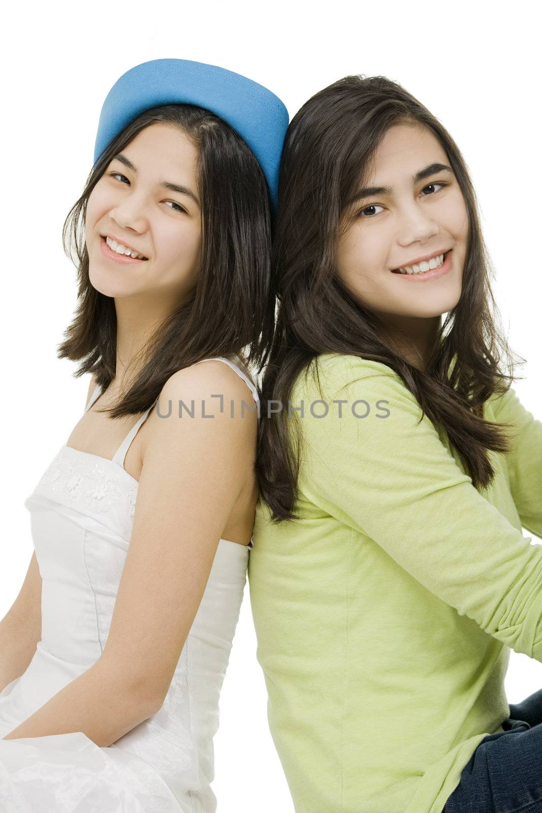 Two young teen girls back to back sitting together, isolated on white