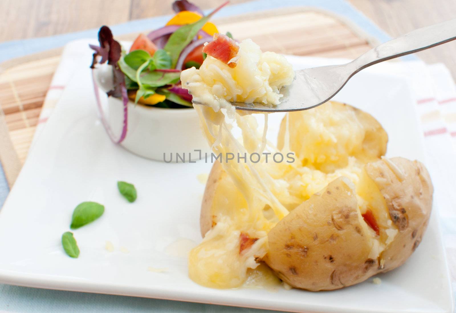 Melting cheese and bacon pieces with baked potato and salad in a bowl