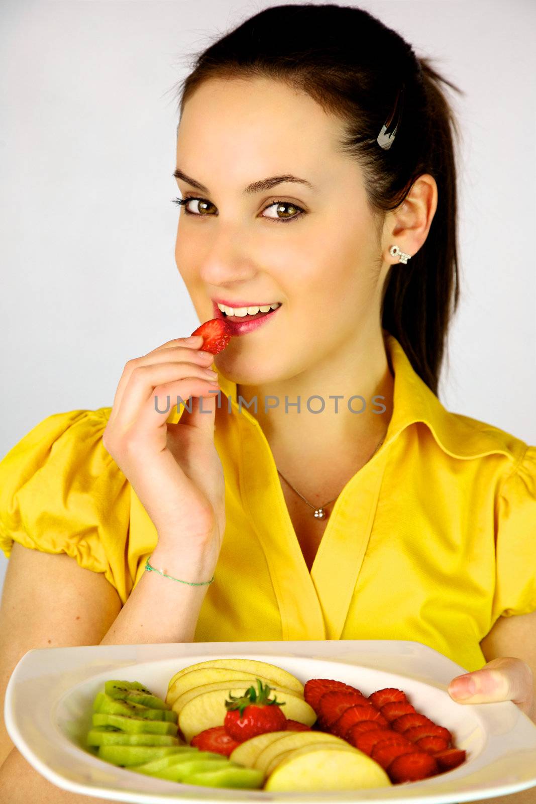 gorgeous brunette female model eating strawberry  with plate full of fruit