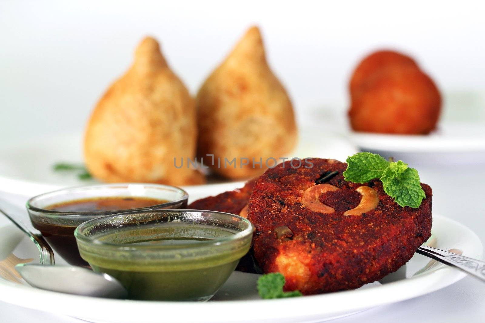Indian deep fried snack cutlet made of potatoes, masala and cashew with chutneys and another popular snack samosa in the background
