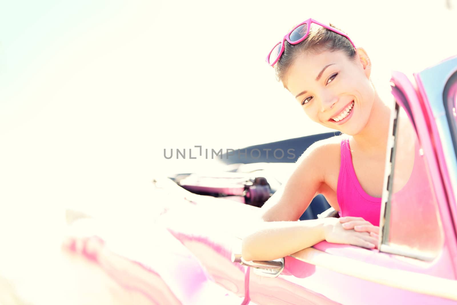 Woman driving vintage retro convertible car in pink. Retro style portrait of young beautiful happy smiling asian woman driver.