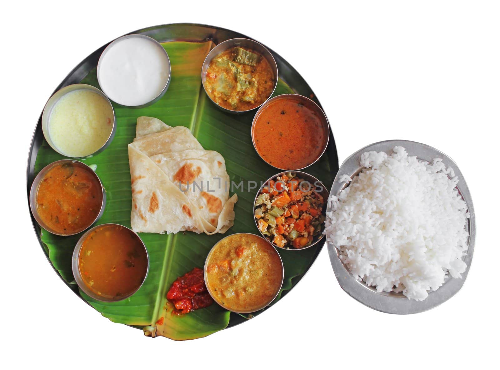 South indian plate meals on banana leaf isolated on white. Traditional vegetarian wholesome indian food with variety of curries, rasam, sambar, rice and chapatti.