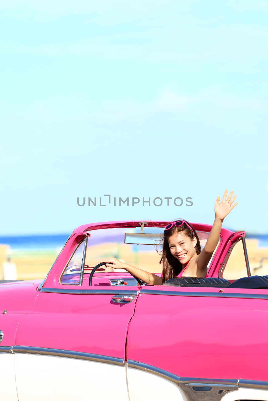 Woman driving convertible retro vintage car waving happy during summer drive. Pretty young multicultural Asian / Caucasian young woman driver.