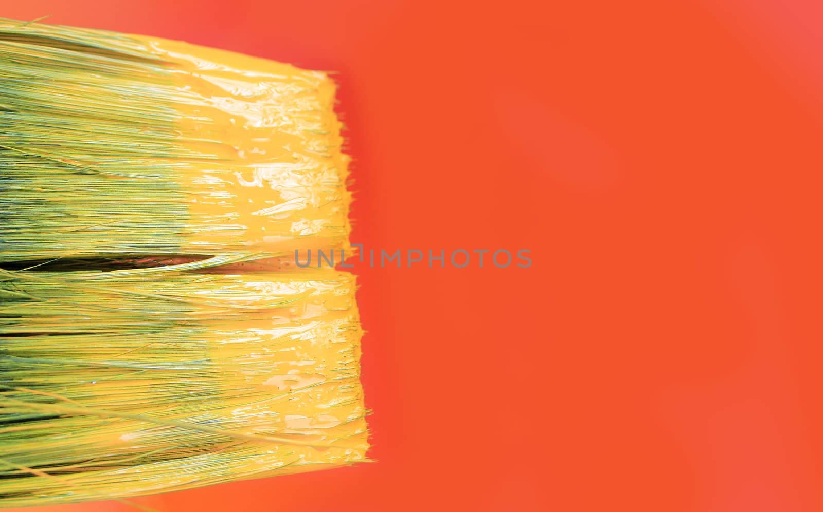 Tip of a paint brush with yellow paint and a orange canvas with copy space in the background