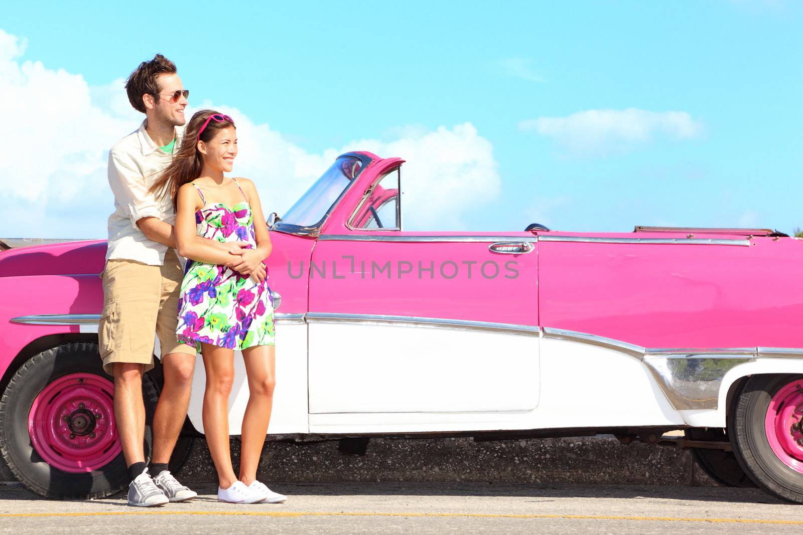 Couple and vintage retro car. Happy smiling young couple standing by pink old vintage car during summer road trip travel in Havana, Cuba. Interracial couple, Asian woman, Caucasian man.