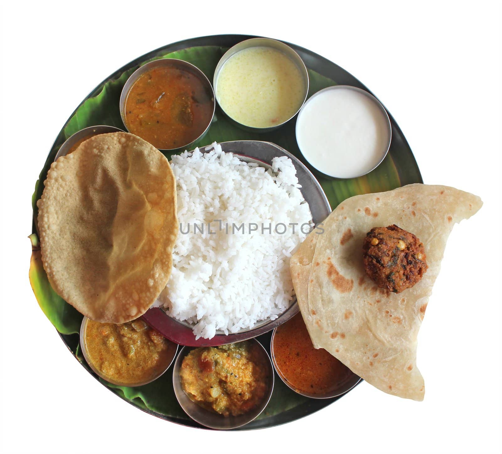 Traditional southern indian plate meals on banana leaf isolated on white. Traditional vegetarian wholesome indian food with variety of curries, rasam, sambar, rice and chapatti.