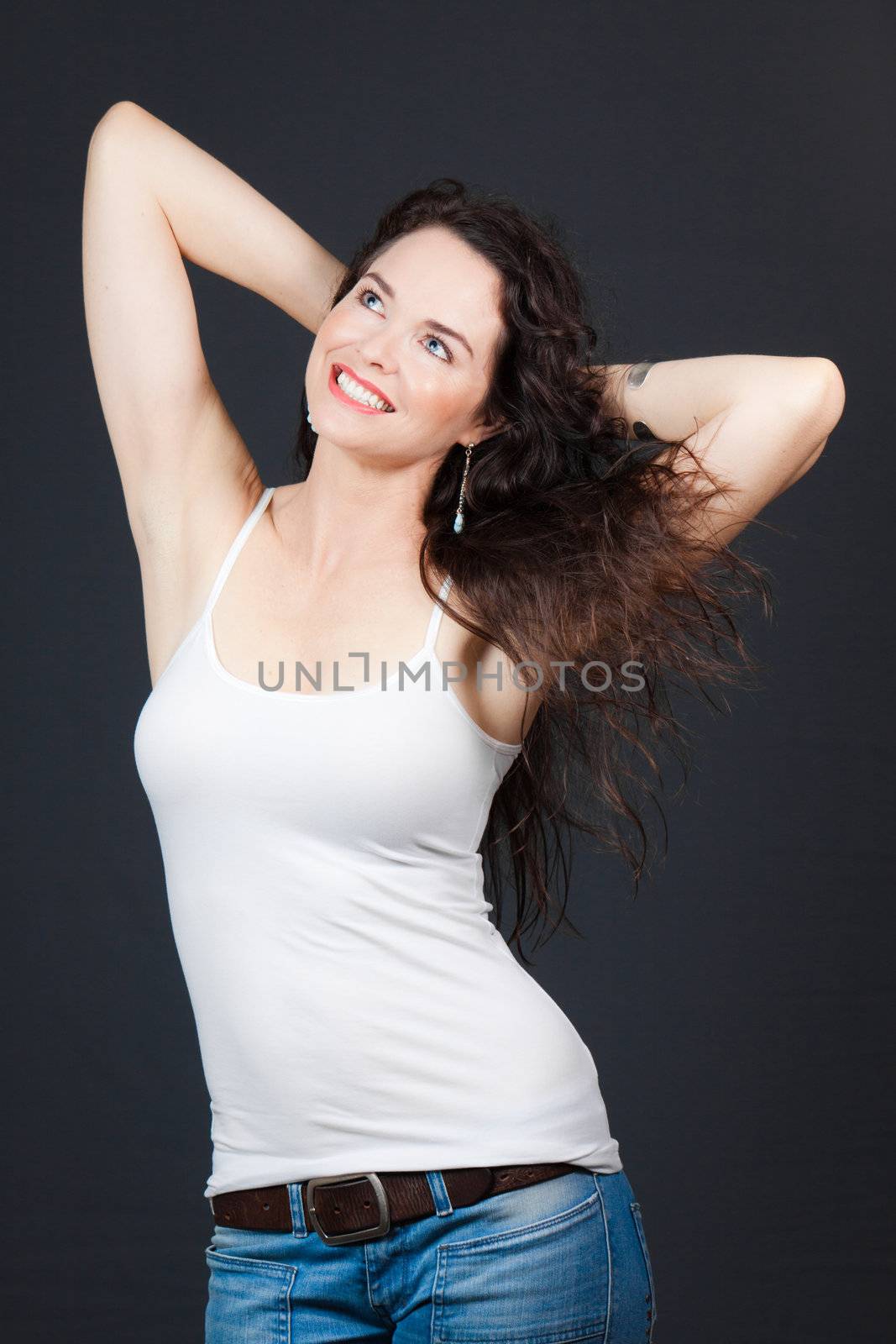 A beautiful young brunette with her hands behind her head, over grey background