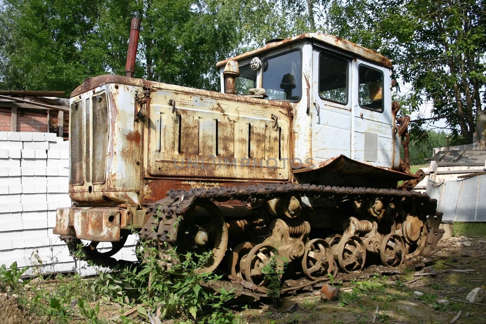 Tractor old in village at a fence from a white brick