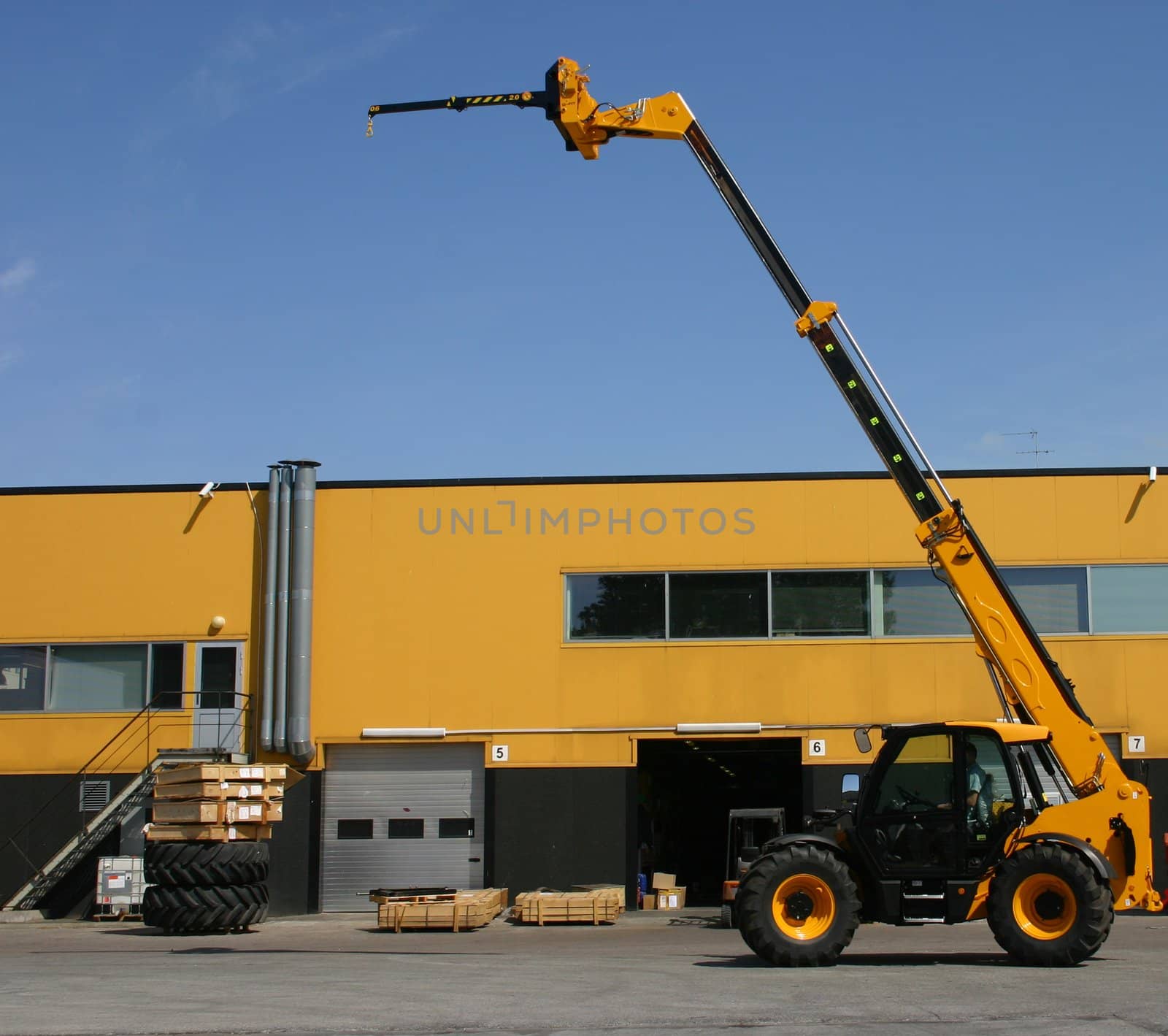Elevating yellow crane near a yellow warehouse