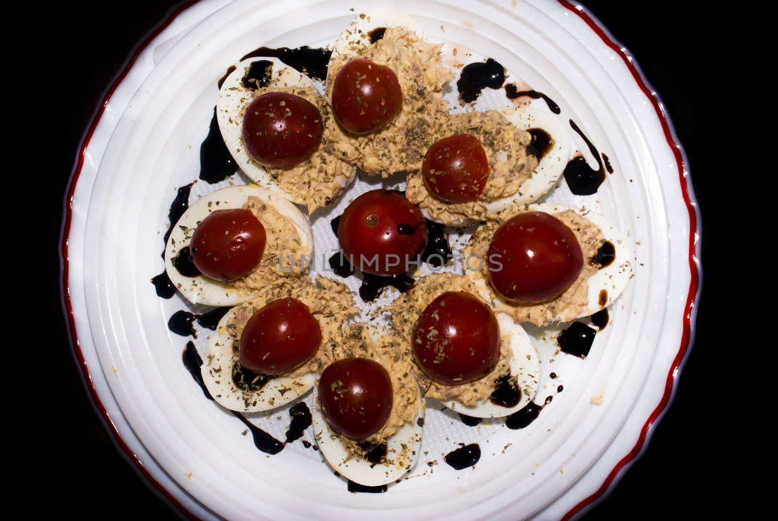 Plate of eggs with tuna and tomato sauce on black background