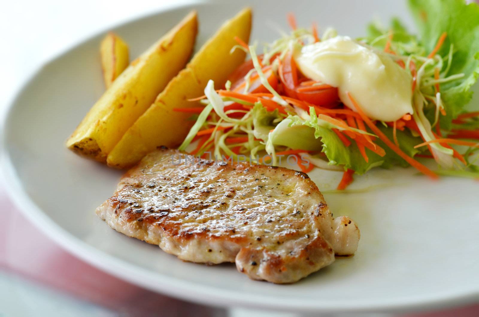 Grilled pork steak served with chips, potatoes and vegetables