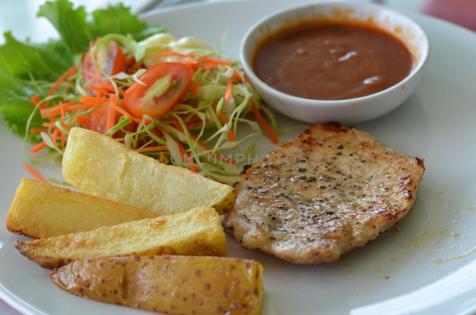 Grilled pork steak served with chips, potatoes and vegetables , tomato sauce