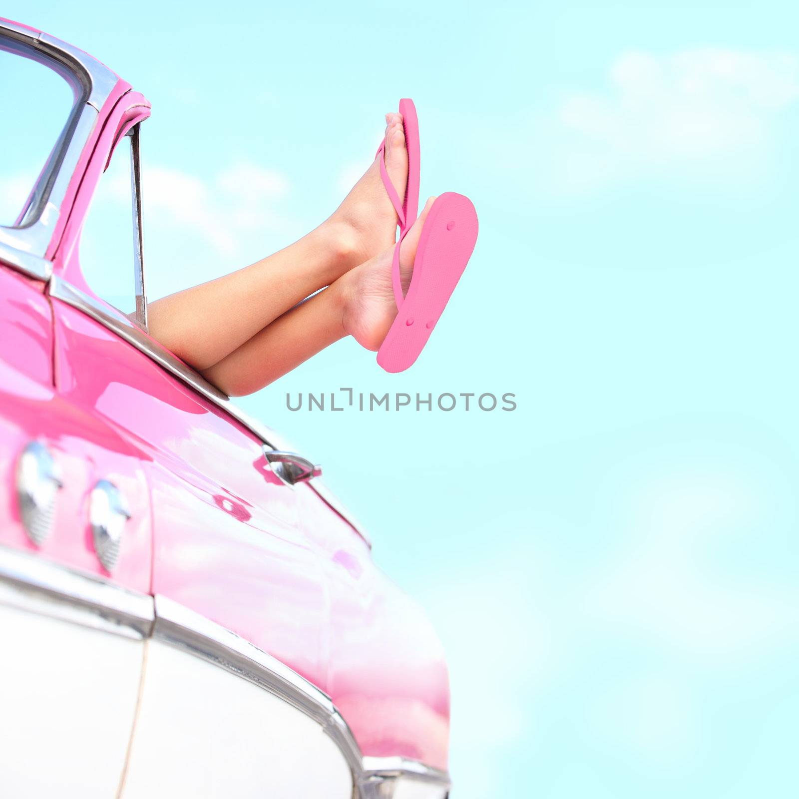Summer fun vintage car. Legs showing from pink vintage retro car. Freedom, travel and vacation road trip concept lifestyle image with woman and copy space on blue sky.