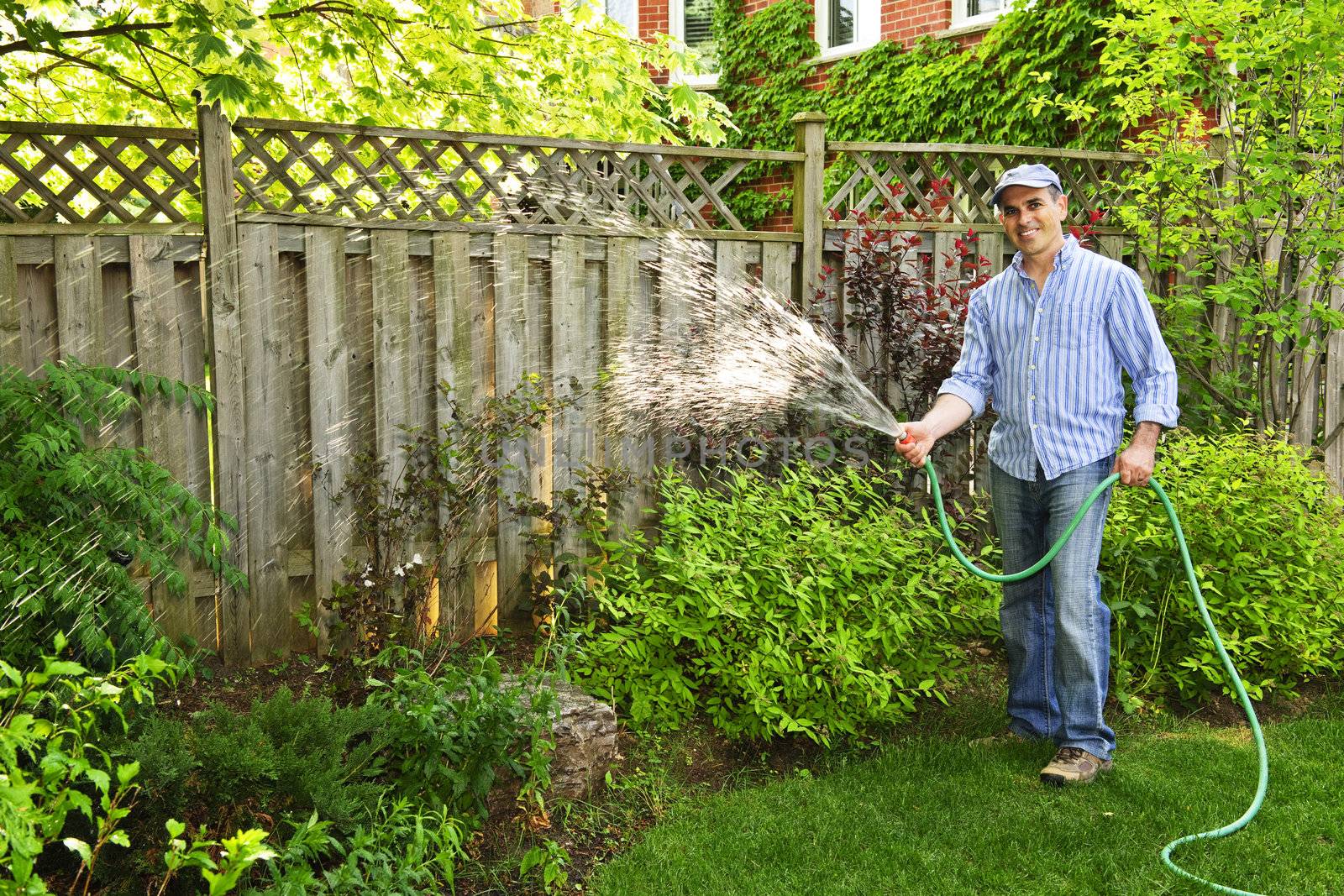 Man watering the garden with hose in backyard