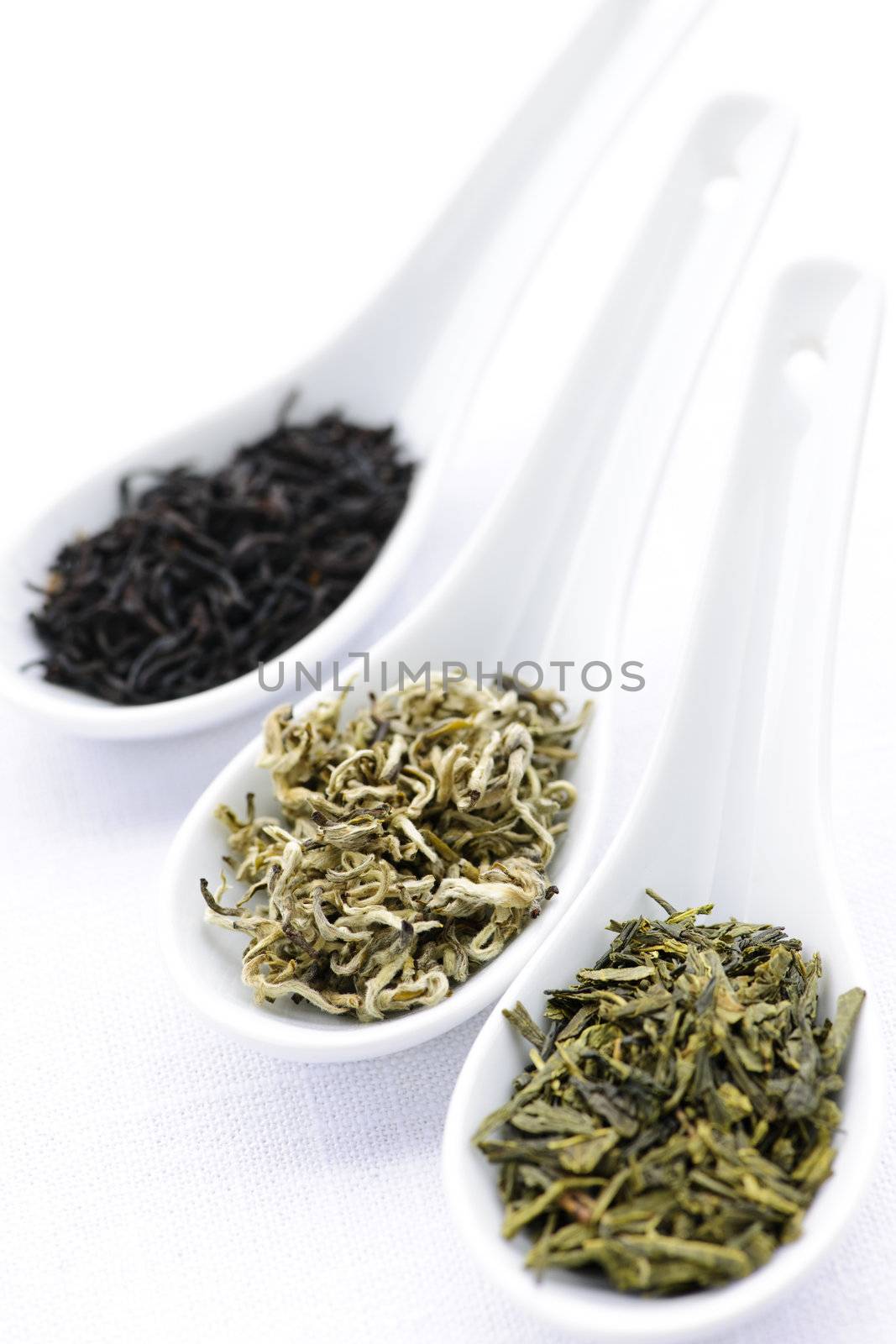 Black, white and green dry tea leaves in spoons