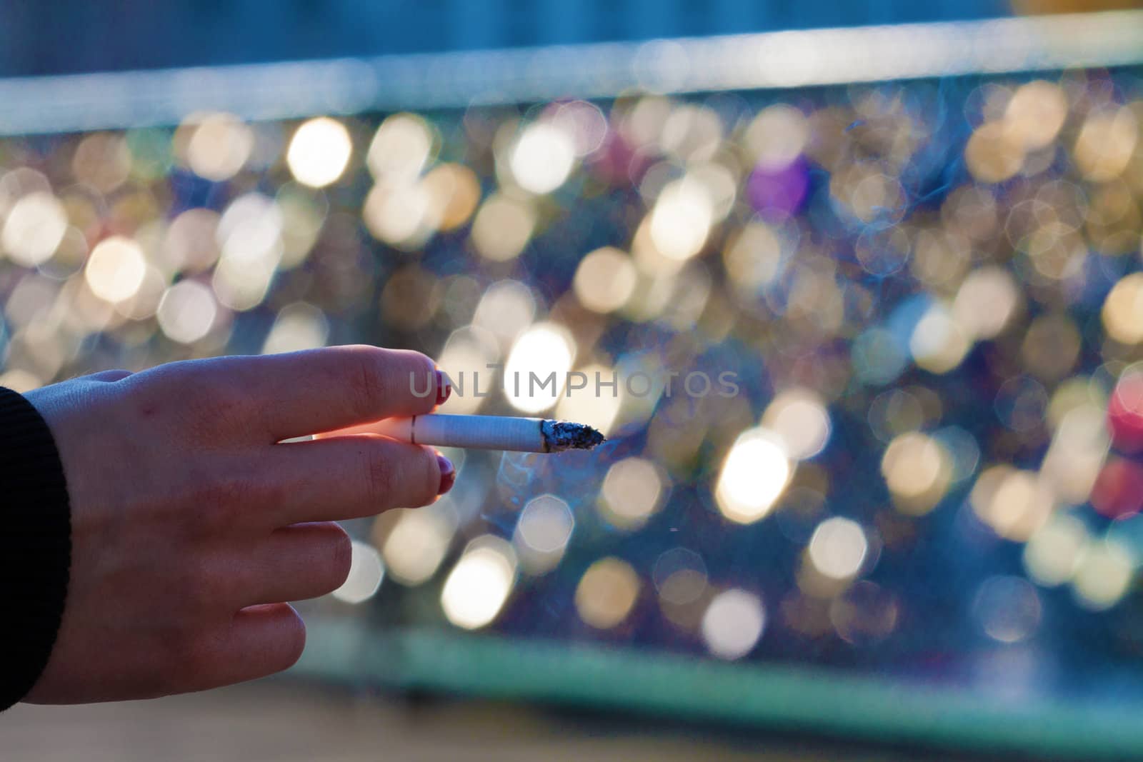 Female hand with a burning cigarette with bokeh of glittering lights