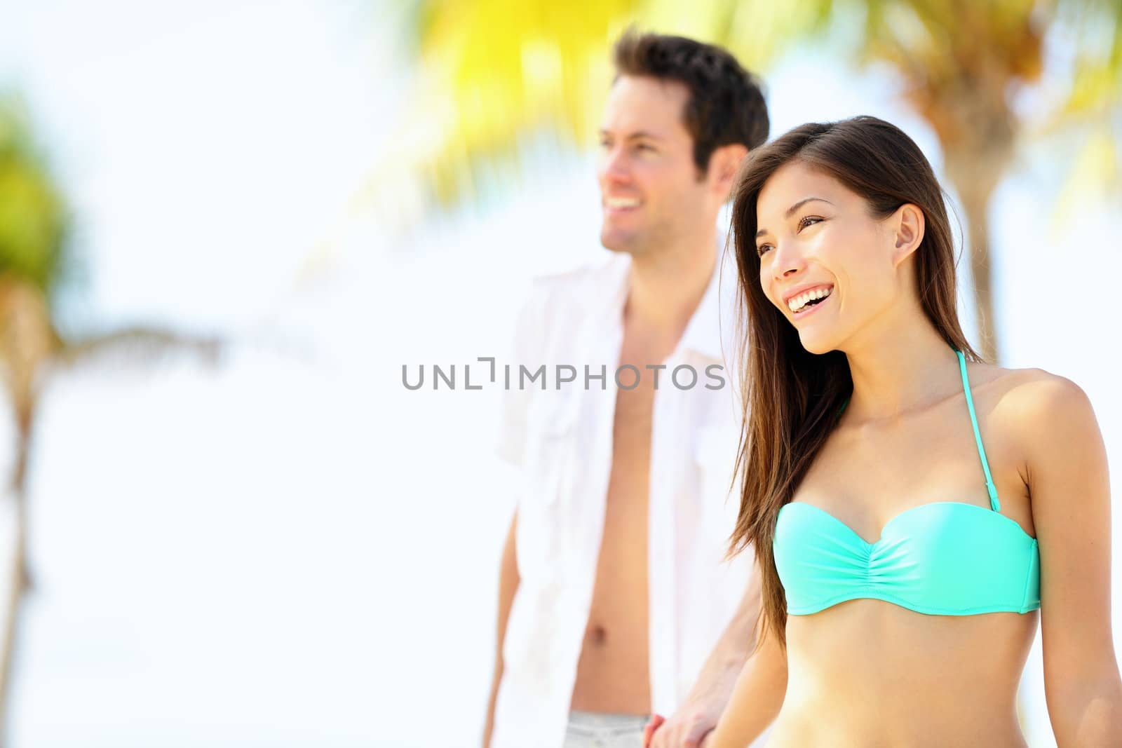Happy couple on beach vacation travel walking under the sun on sunny summer day. Young beautiful interracial couple, Asian woman, Caucasian man.