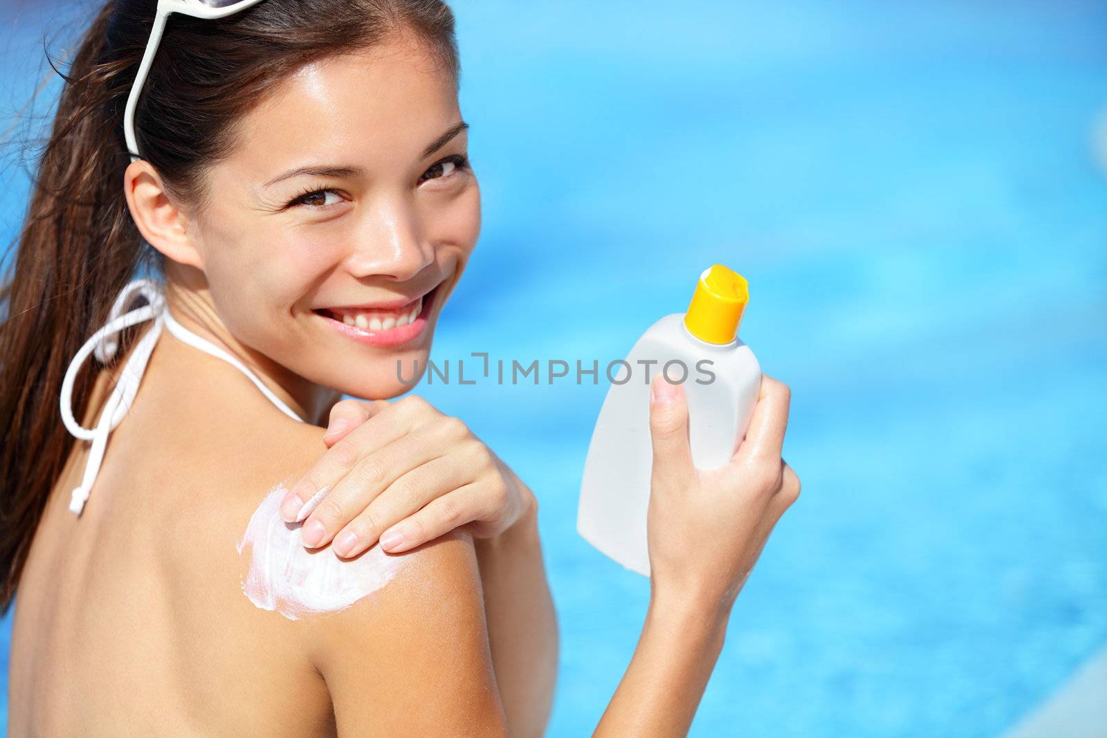 Sunscreen / sunblock. Woman putting solar cream on shoulder smiling happy outdoors by pool under sunshine on beautiful summer day. Mixed race Asian / Caucasian girl.