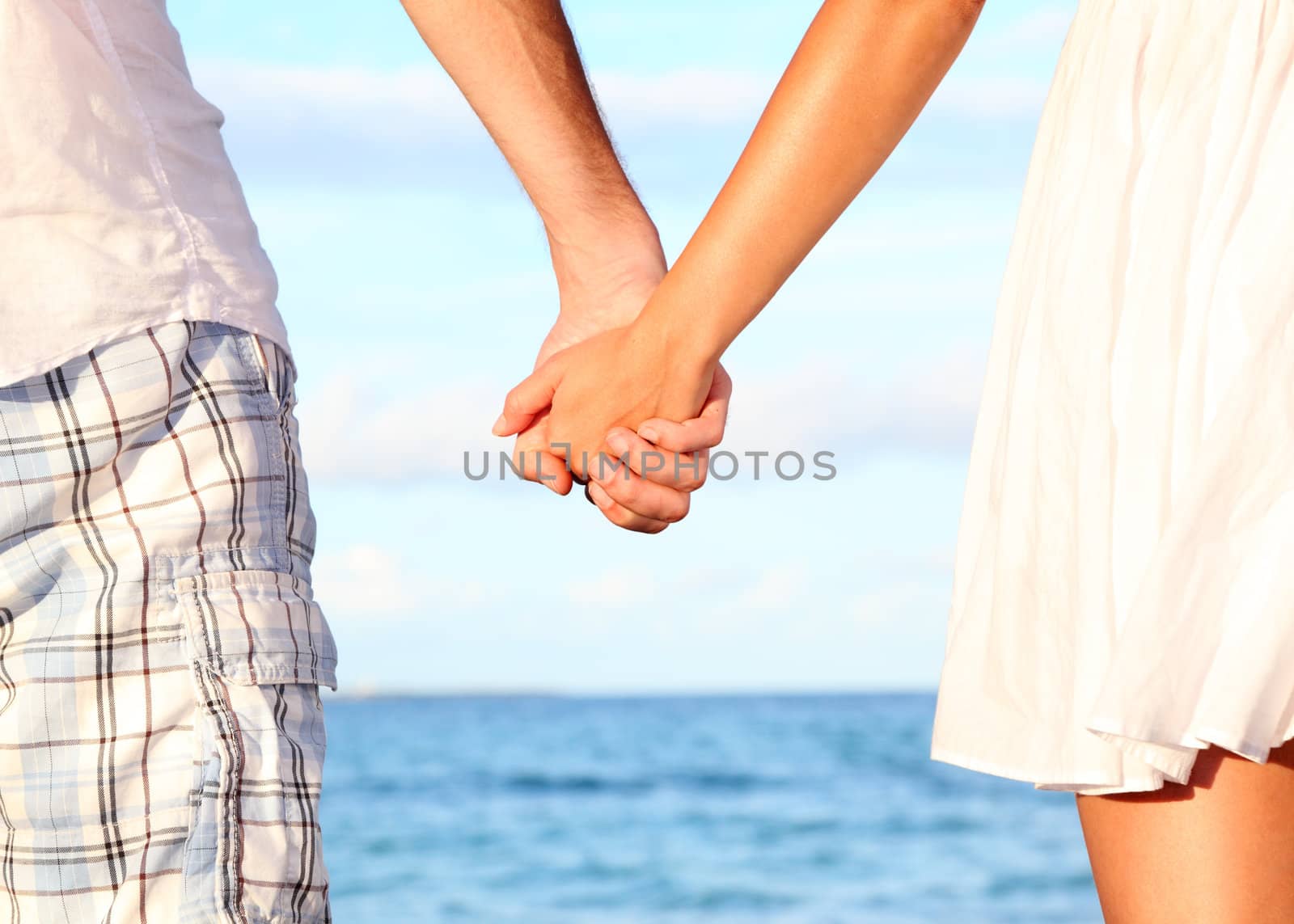 Holding hands couple on beach. Romantic love and happiness concept image with happy young couple. Closeup.