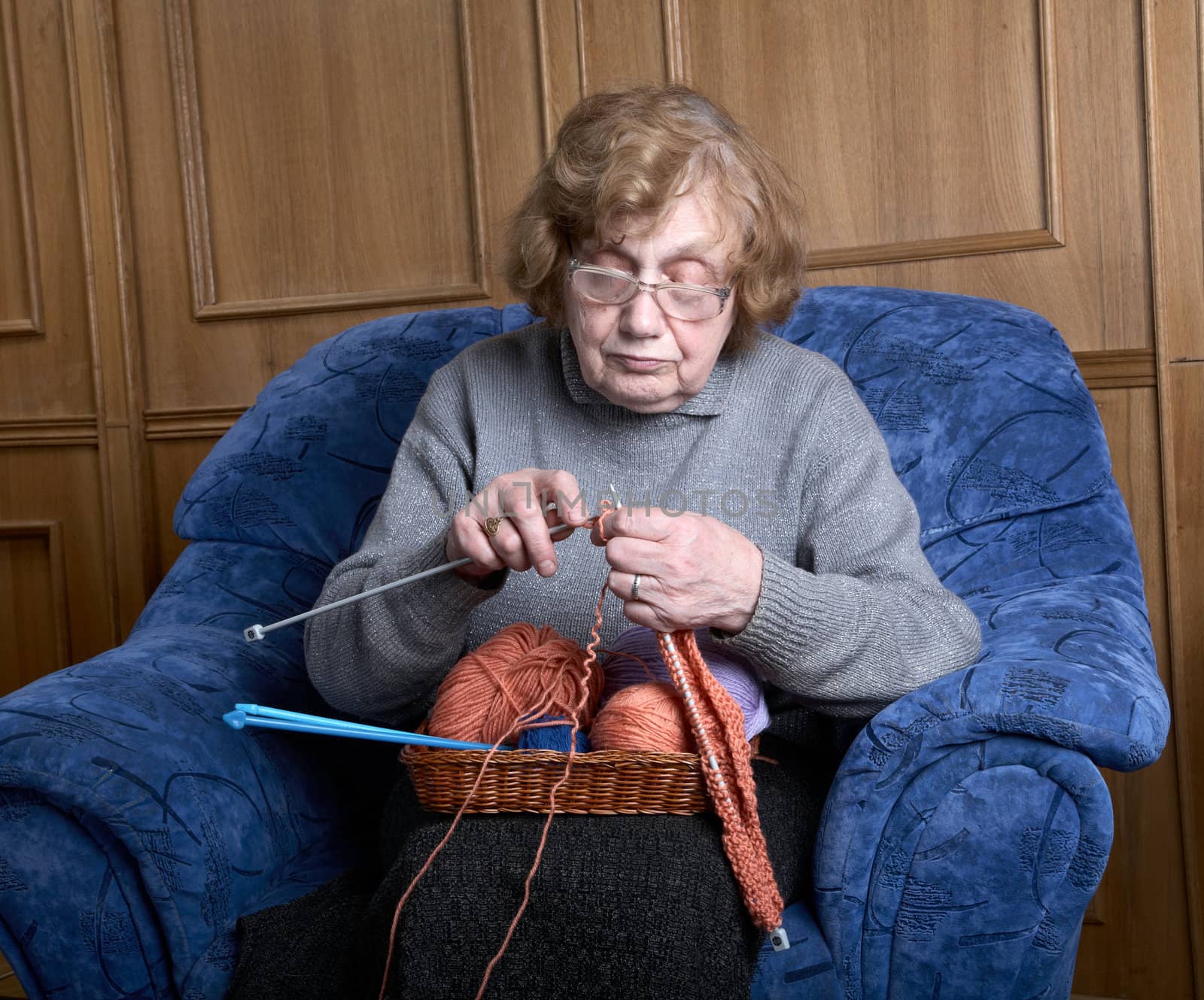 The old woman sits in an armchair and knits