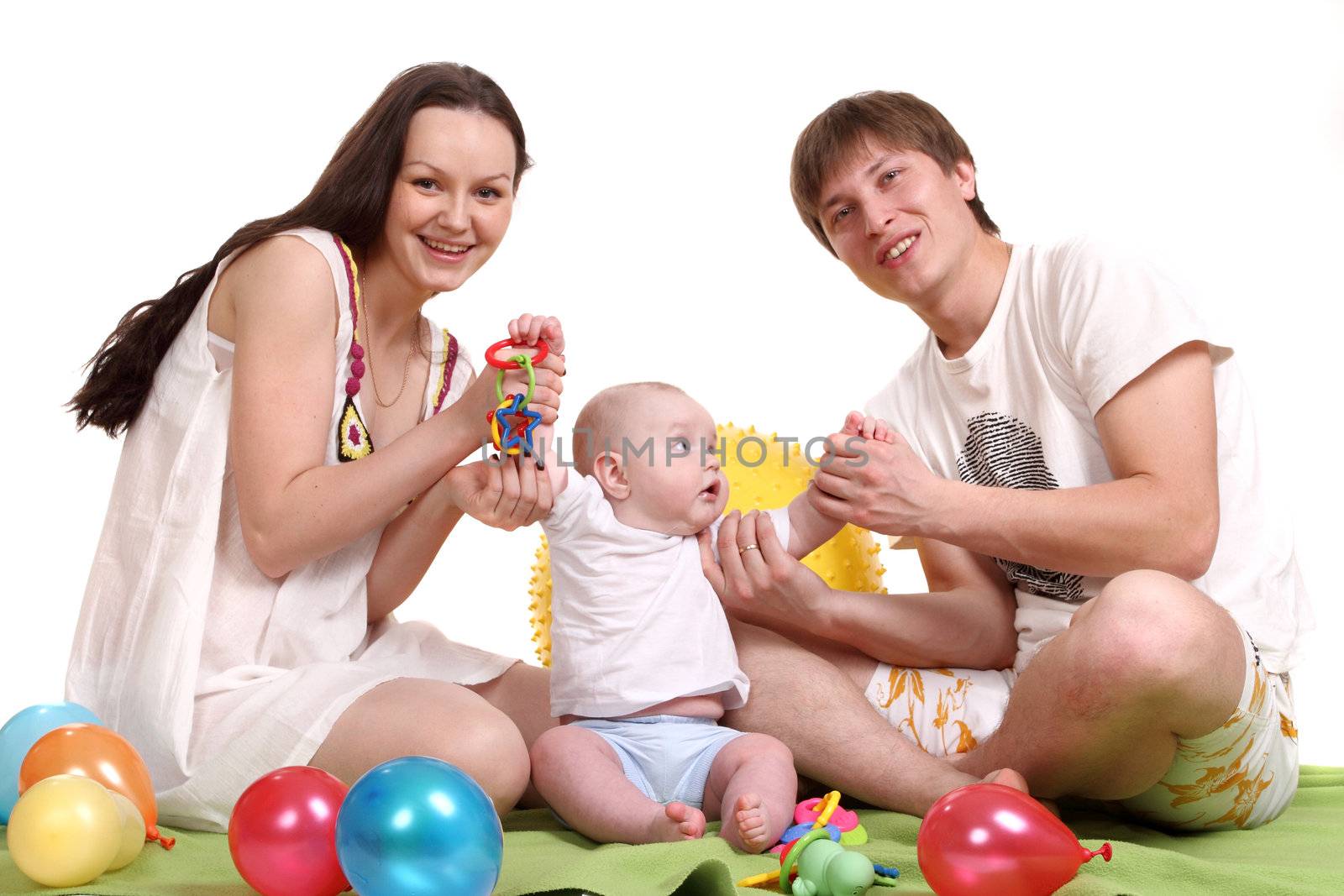 The young family, mum, the father and the son sit on a green plaid and play multi-colored balls