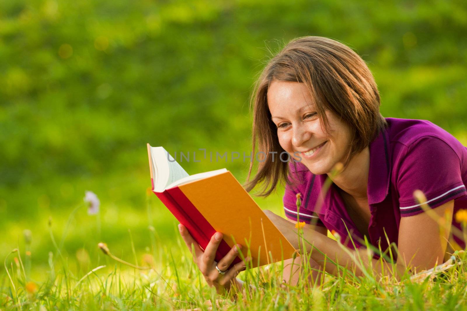 Beautiful woman laughing with a book in the park by Lamarinx