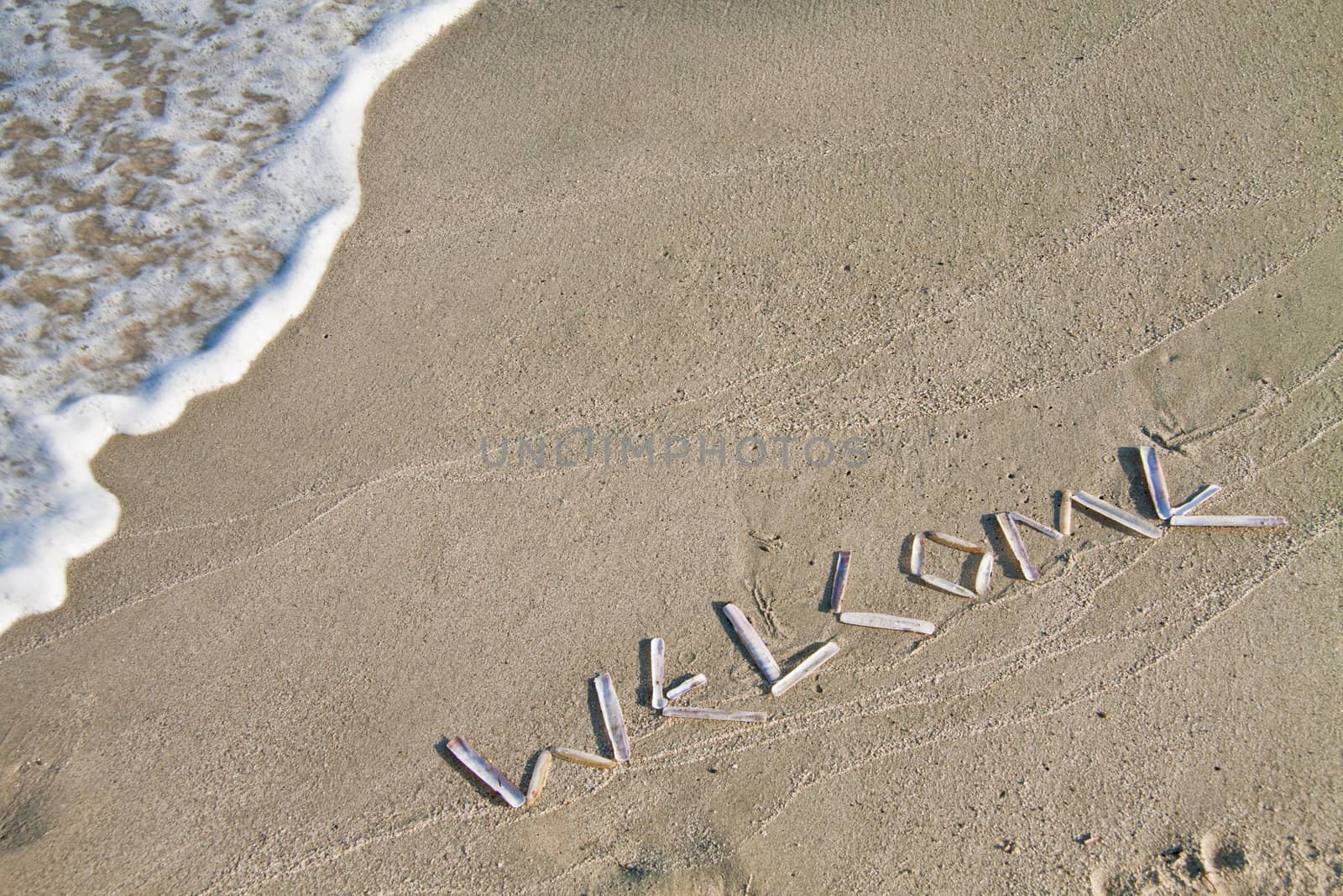 Welcome sign written with shells on the beach.