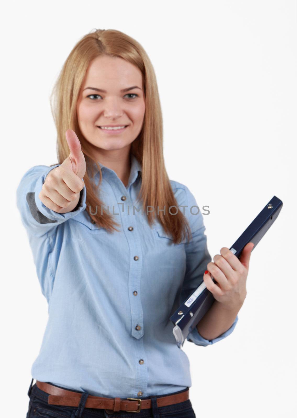 Portrait of an optimistic student blonde girl with her right thumb up and holding a folder in her left hand.The focus is selective on her thumb.