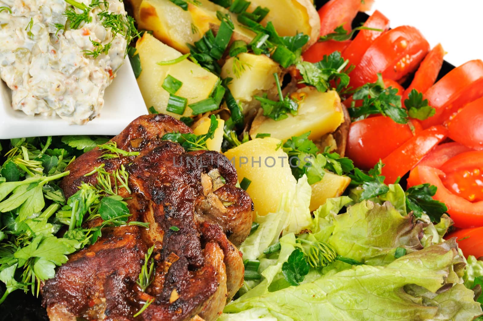 Grilled meat and potatoes. Decorated with tomatoes, lettuce and herbs.