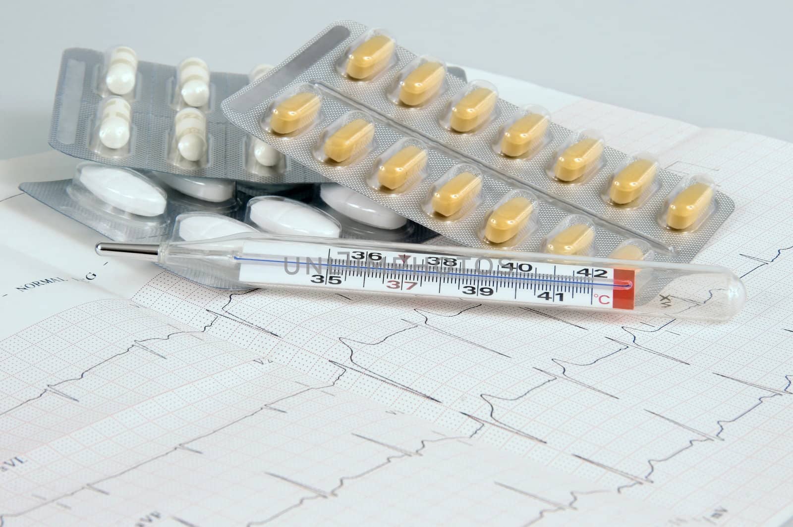 Three kinds of tablets on electrocardiogram sheet with a thermometer