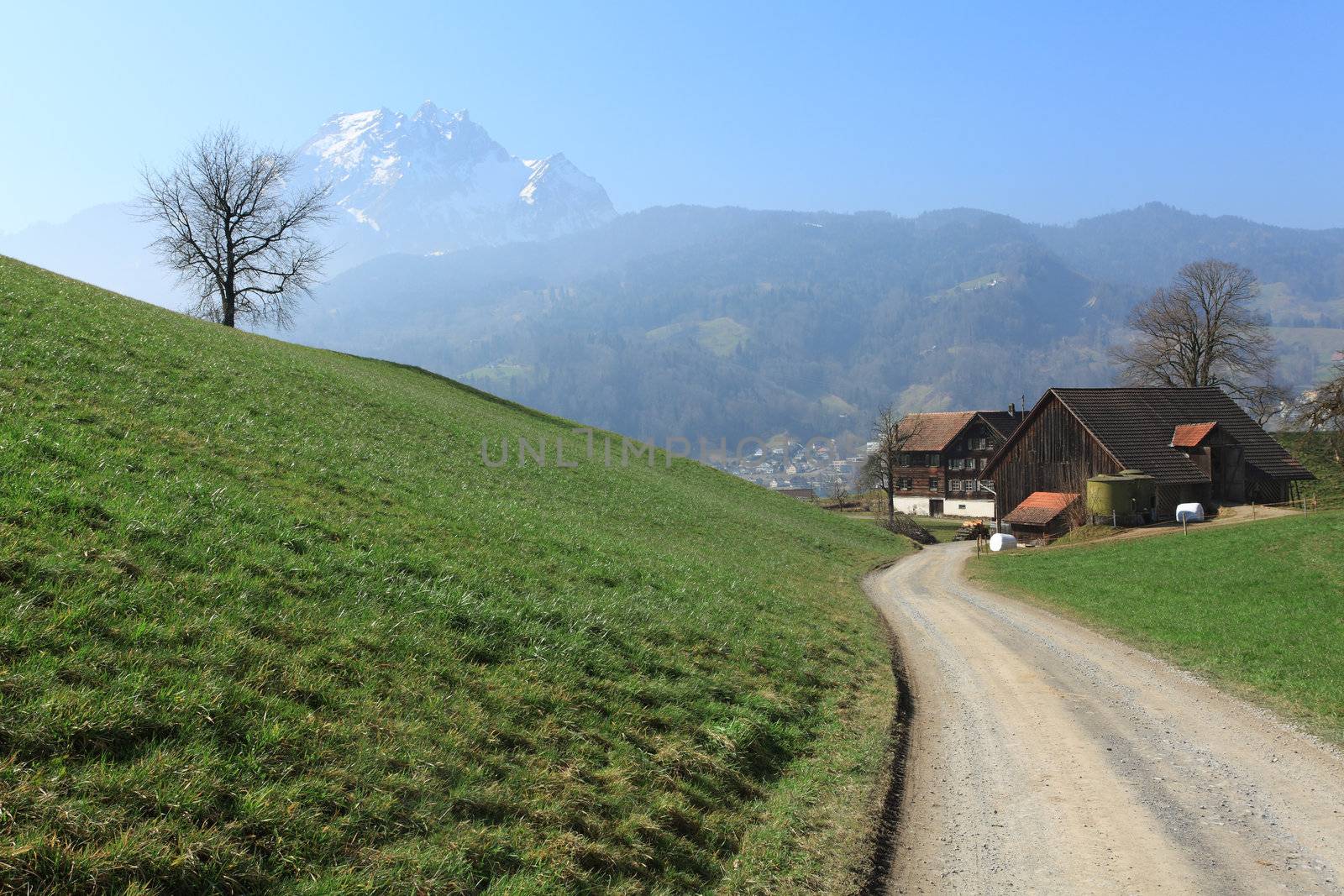 Photo of a road leading towards a farm in the Canton of Lucerne, Switzerland with the Pilatus mountain in the distance.