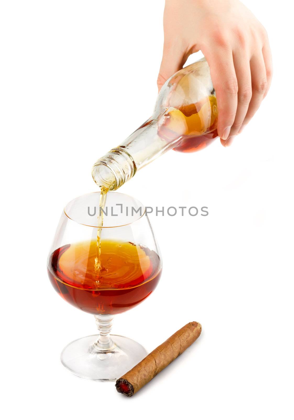 Pouring of cognac in glass with cigar isolated on white background