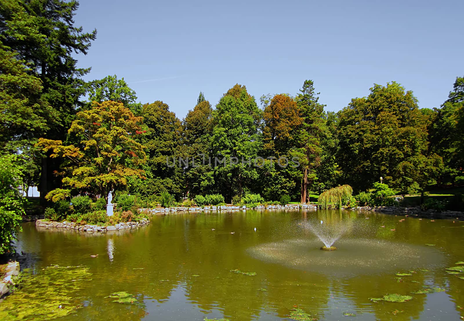 A photograph of a statue and fountain at a lake in a public park.