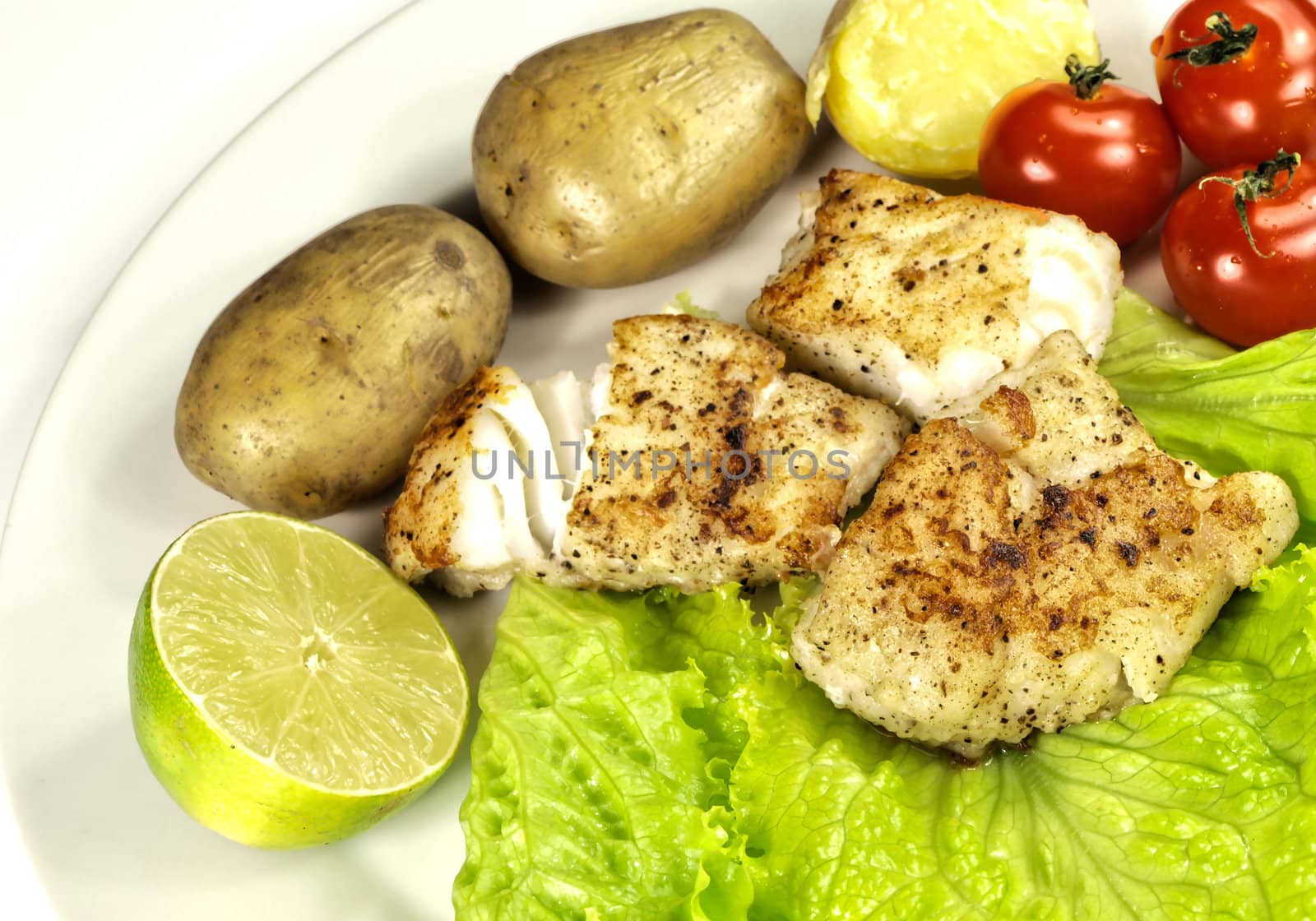 Fried white fish on a plate, with potatoes, salad, lime and tomatoes